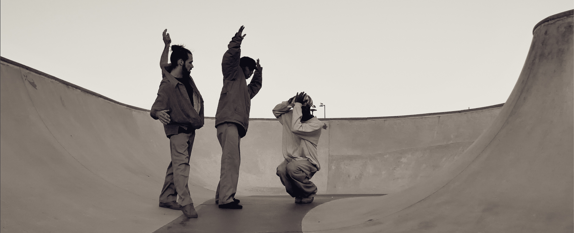 Trois danseurs bras levés, dont un accroupi, sur la courbe d'un skatepark